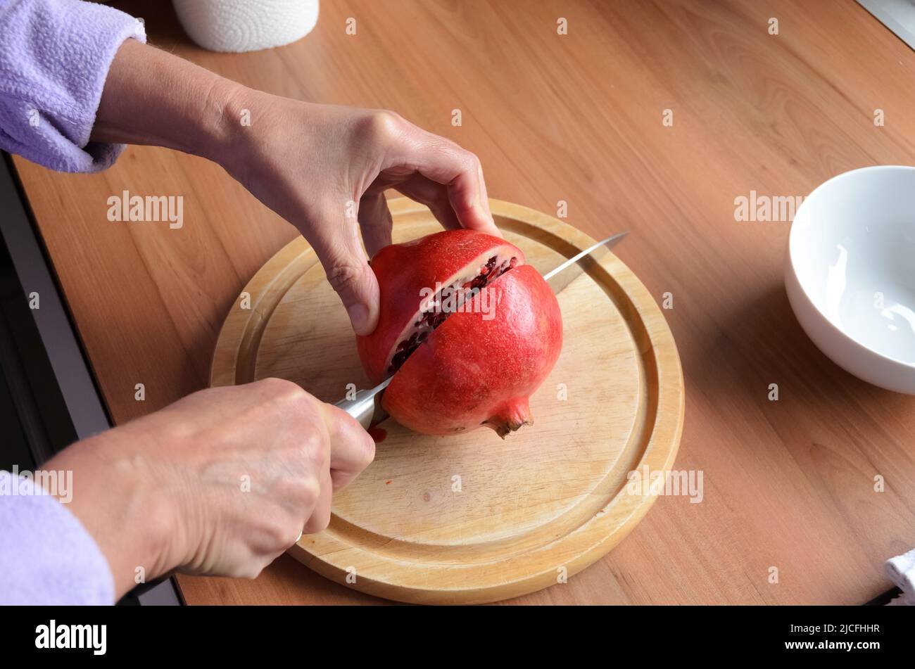 Couper et ouvrir un fruit grenade rouge (Punica granatum) avec un couteau sur une planche en bois Banque D'Images