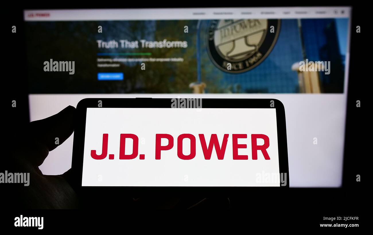 Personne tenant un téléphone portable avec le logo de la société américaine de recherche sur les consommateurs J.D. Power à l'écran en face de la page Web. Mise au point sur l'affichage du téléphone. Banque D'Images