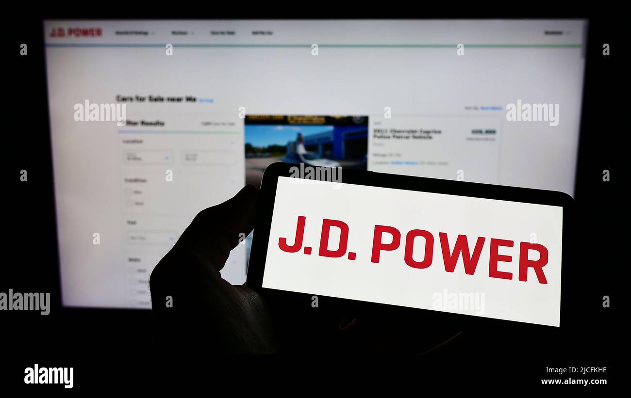Personne tenant un téléphone portable avec le logo de la société américaine de recherche sur le consommateur J.D. Power sur l'écran devant la page Web d'affaires. Mise au point sur l'affichage du téléphone. Banque D'Images