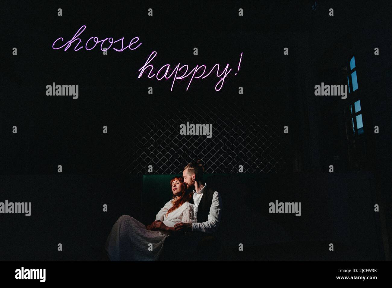 Un jeune couple amoureux assis sous un panneau au néon « Choose Happy! » Banque D'Images