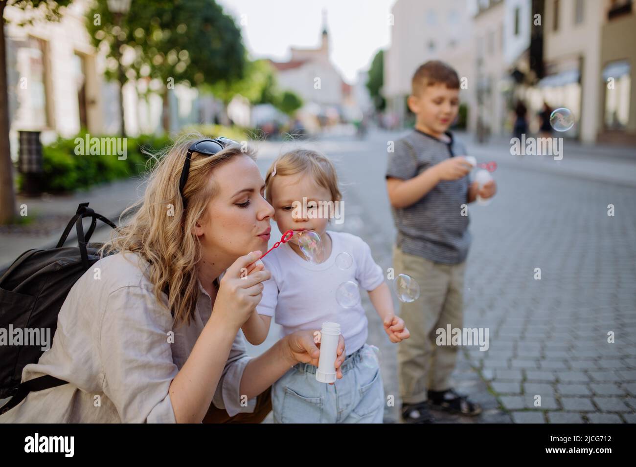 Jeune mère jouant avec ses enfants, en soufflant des bulles dans la rue de la ville en été. Banque D'Images