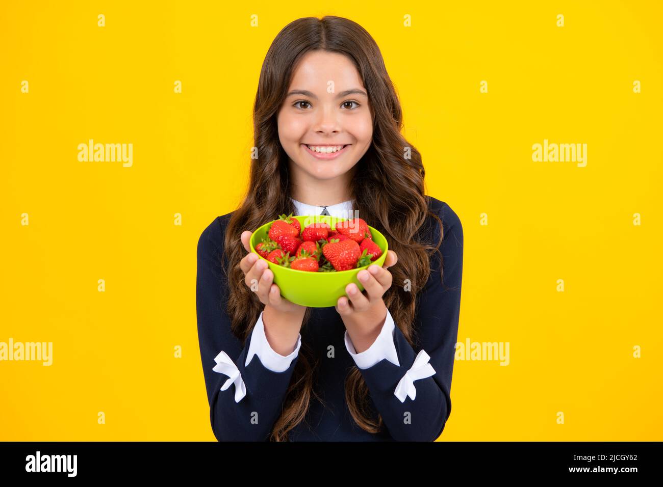 Un enfant de l'adolescence tient un bol à fraises sur fond jaune. Banque D'Images