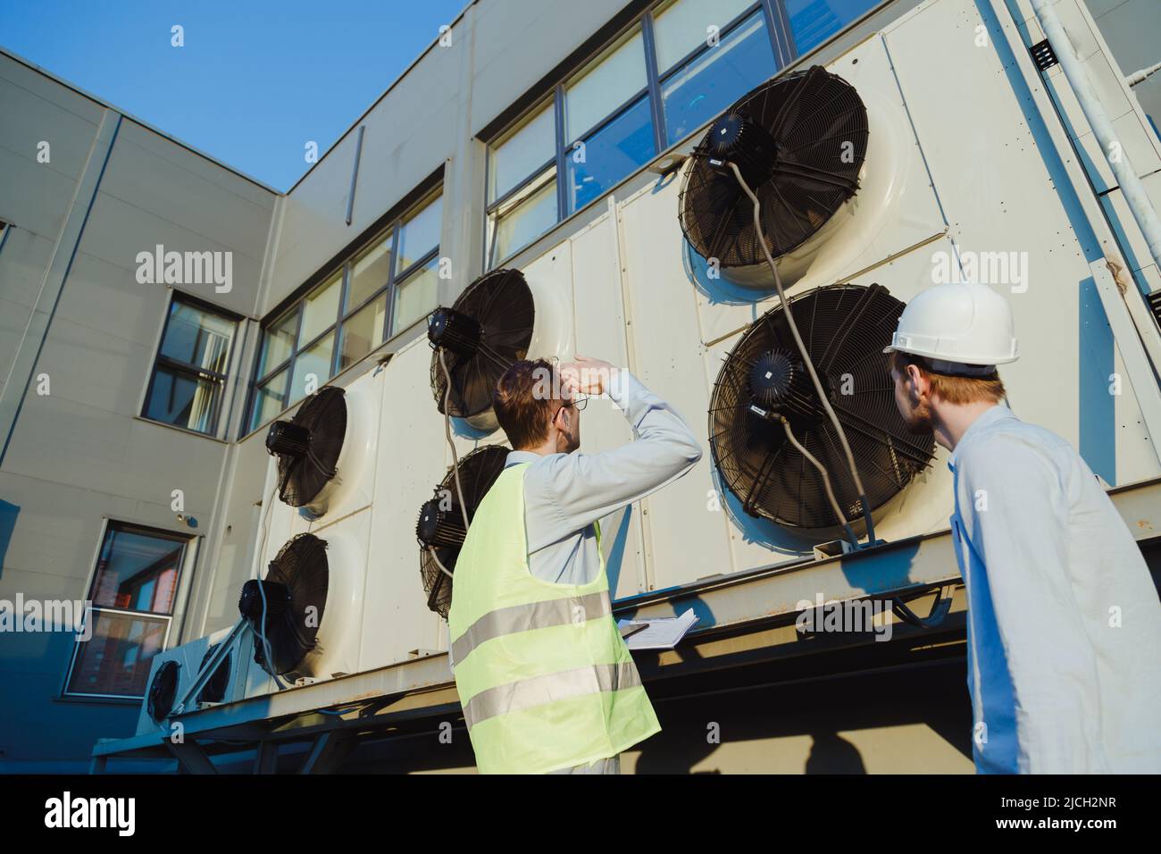 Réunion d'architecte et de superviseur sur le chantier de construction. Discussion sur le plan. Deux ouvriers de la construction travaillent ensemble au service d'entretien des réfrigérateurs hvac Banque D'Images