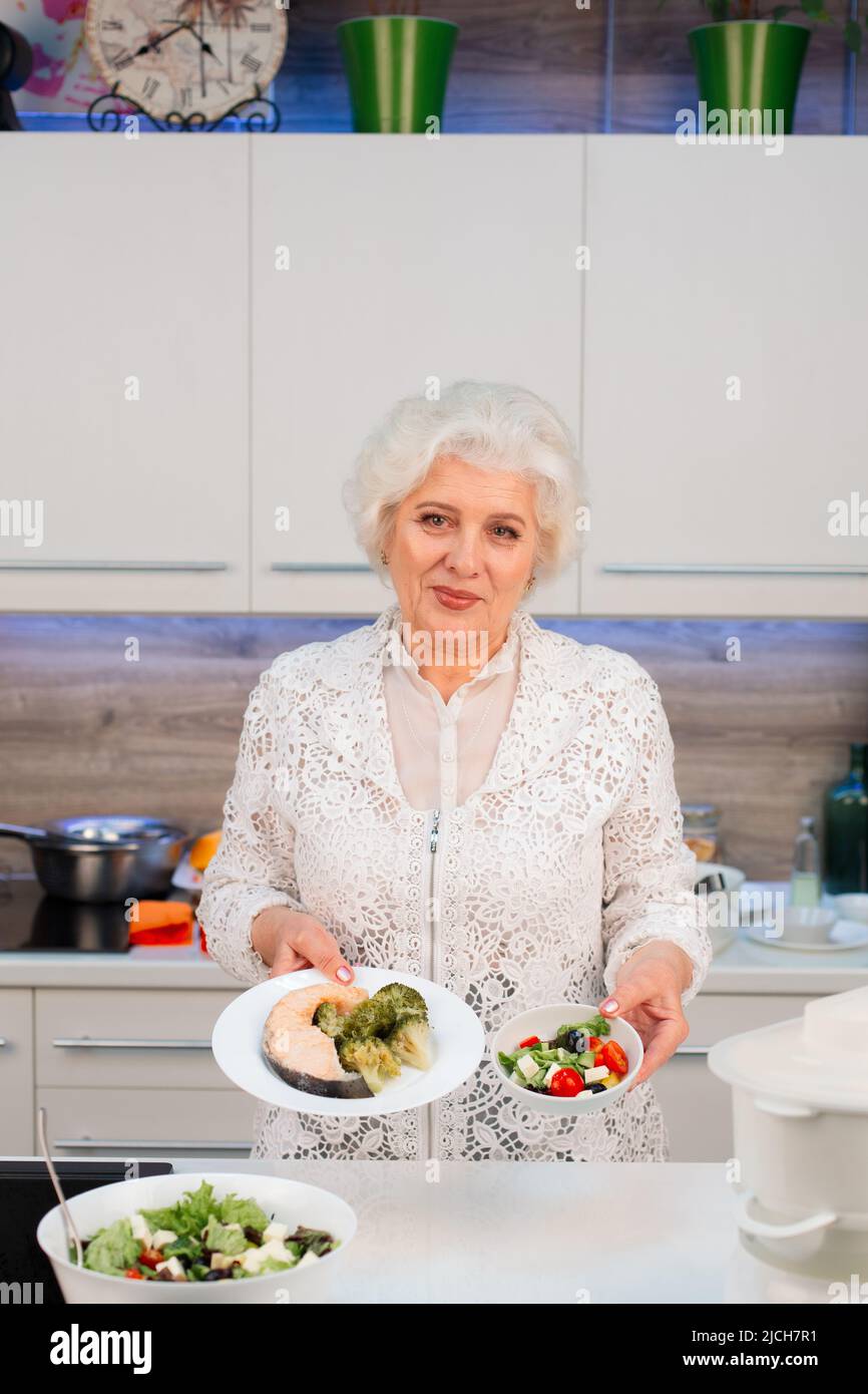 Un pensionné cuisine des aliments sains dans la cuisine, montre des plats cuisinés Banque D'Images