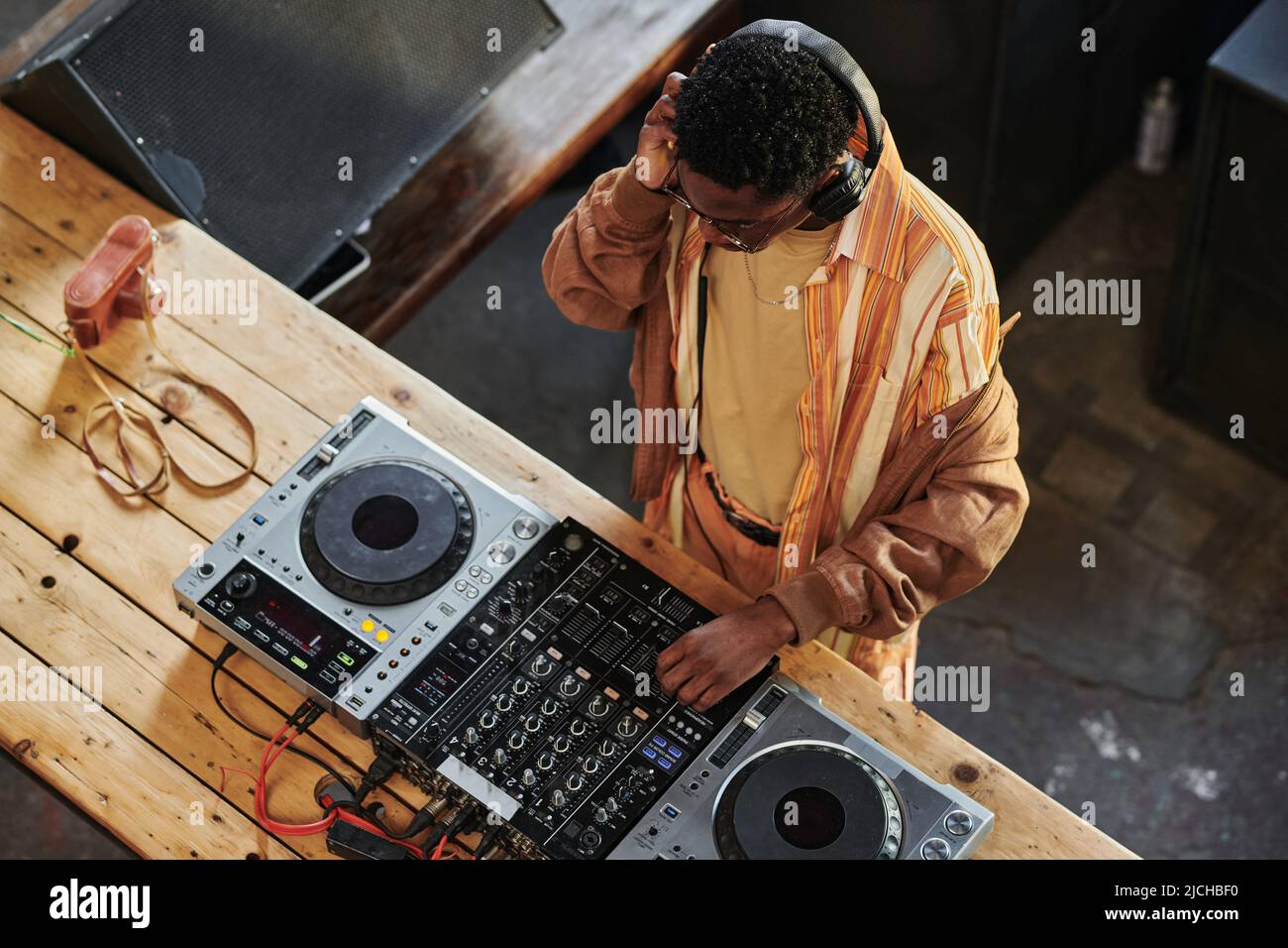 Un homme afro-américain avec casque mixant des sons sur dj et faisant de la nouvelle musique tout en se tenant debout près d'une table en bois dans le studio Banque D'Images