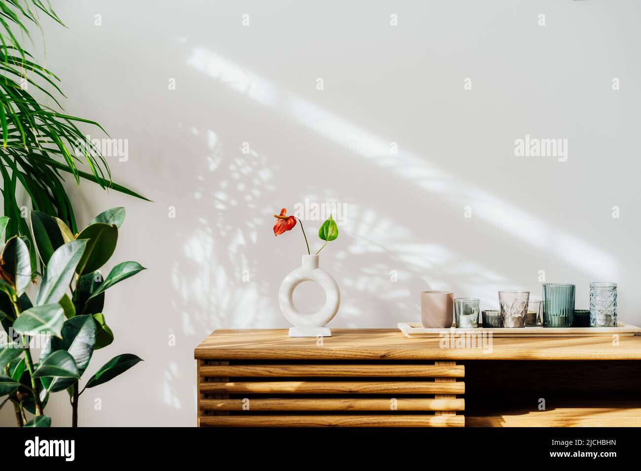 Intérieur moderne et minimaliste de style scandinave. Vase en céramique nordique avec fleur d'Anthurium rouge, bougies sur une console en bois. Plantes de maison vertes en pots Banque D'Images