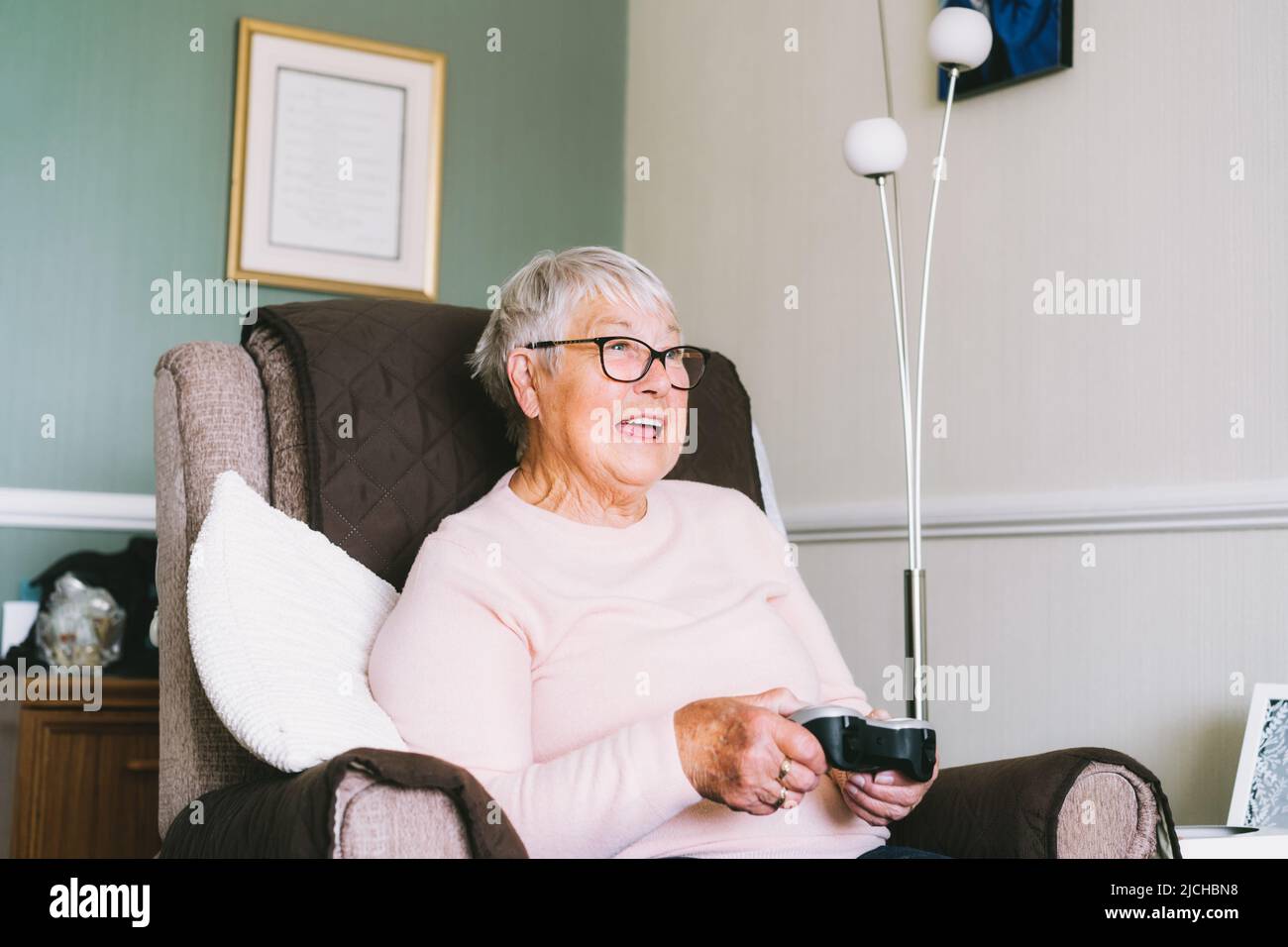 Emotive senior, femme mature regardant l'écran de télévision et utilisant la manette sans fil, manette de jeu jouant des jeux vidéo à la maison. Amusez-vous à la retraite. AG Banque D'Images Emotive senior, femme mature regardant l'écran de télévision et utilisant la manette sans fil, manette de jeu jouant des jeux vidéo à la maison. Amusez-vous à la retraite. AG Banque D'Images