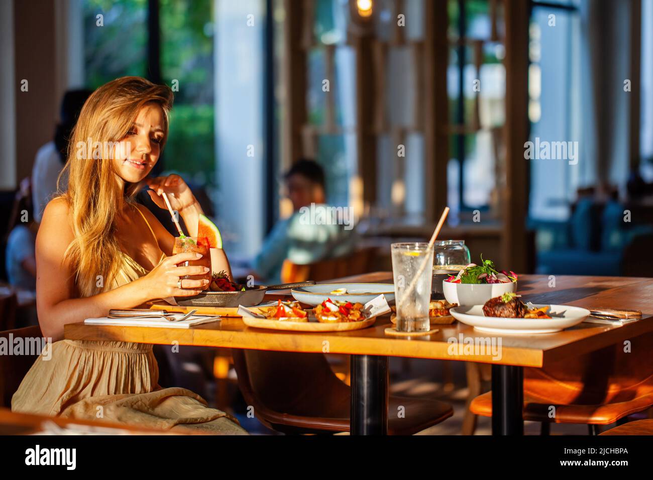 Belle et heureuse fille appréciant un dîner romantique avec des cocktails dans un restaurant luxueux pendant le coucher du soleil. Jeune femme attrayante avec de longs cheveux Banque D'Images