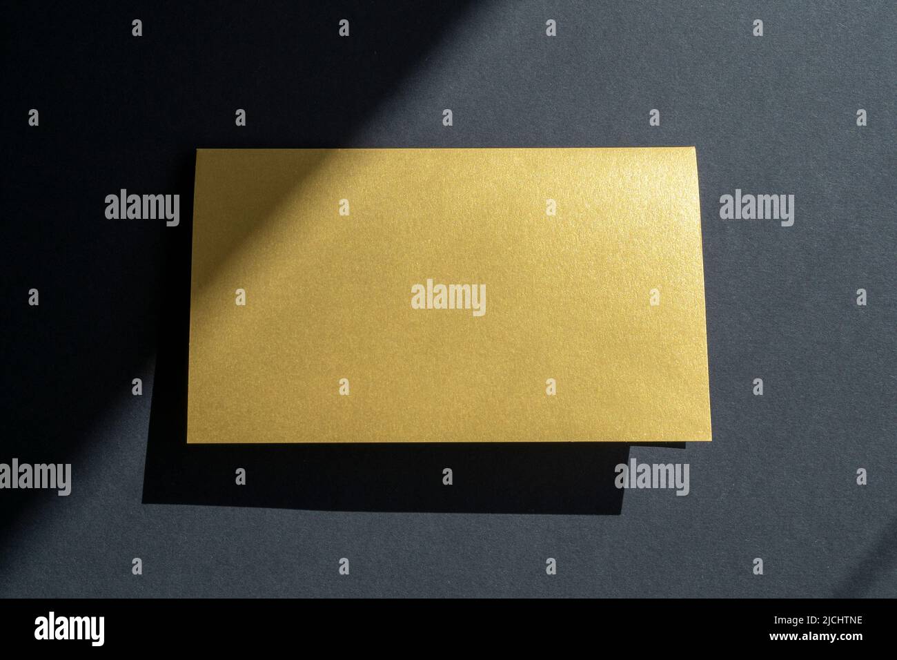 Maquette de carte de visite dorée, invitation sur surface noire avec ombres et lumière du soleil Banque D'Images