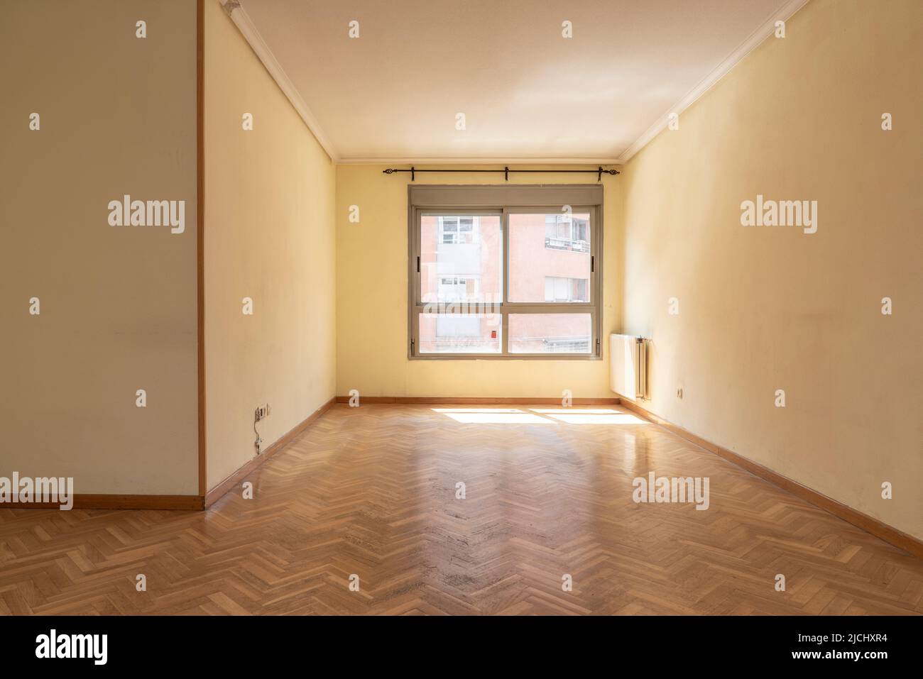 Séjour vide avec parquet en chêne, radiateur en aluminium dans un coin et fenêtre en aluminium marron Banque D'Images