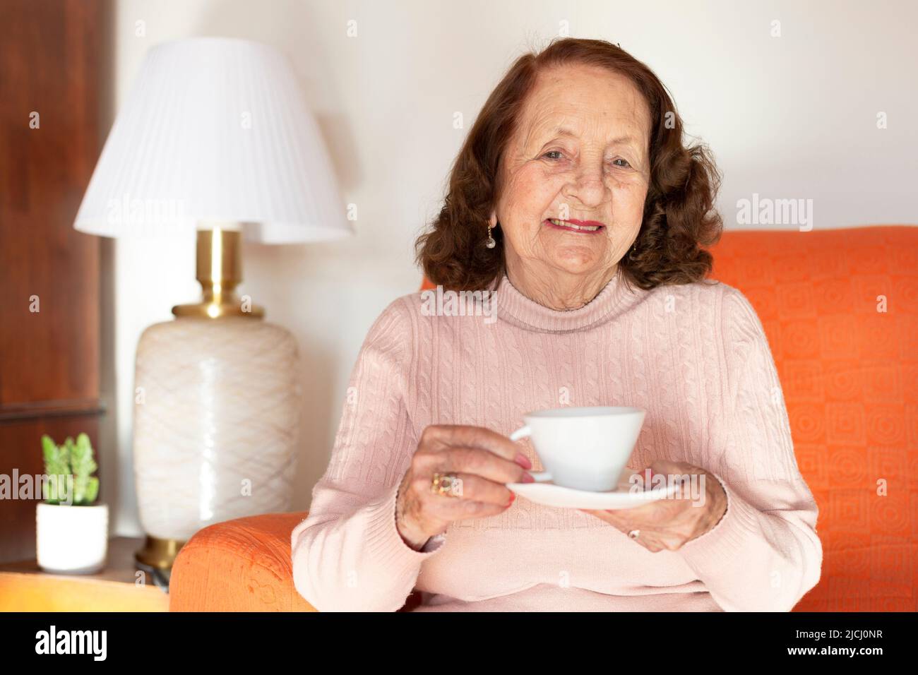 Souriante femme de race blanche qui boit du café ou du thé à la maison. Mode de vie des personnes âgées. Banque D'Images