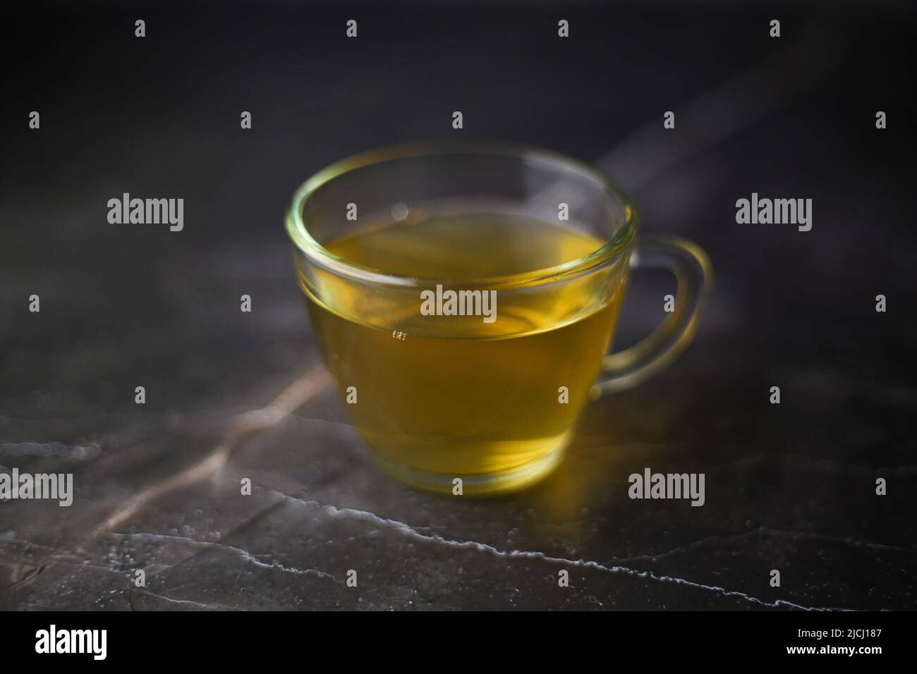 Thé vert infusé éclairé dans une tasse transparente sur fond sombre Banque D'Images