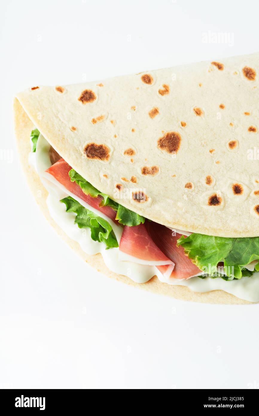 Cuisine italienne de rue plat avec piadina isolé sur un fond blanc. Piadina romagnola - pain plat italien au prosciutto, salade et crème de fromage Banque D'Images