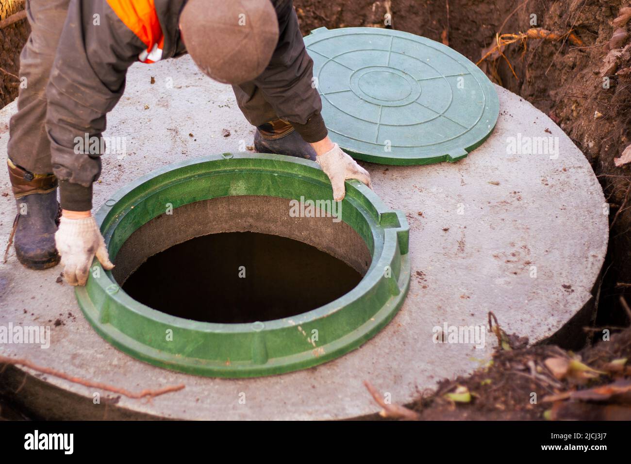 le constructeur installe un trou d'homme sur un puits d'égout en béton. Construction d'une fosse septique pour une maison de campagne. Banque D'Images