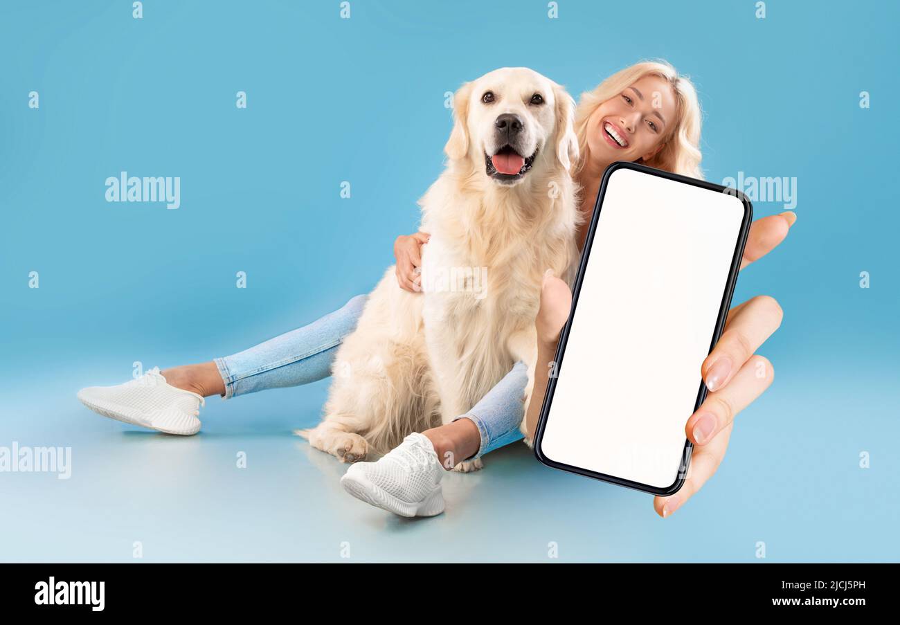 Belle jeune femme assise avec son chien et montrant un grand smartphone vierge Banque D'Images