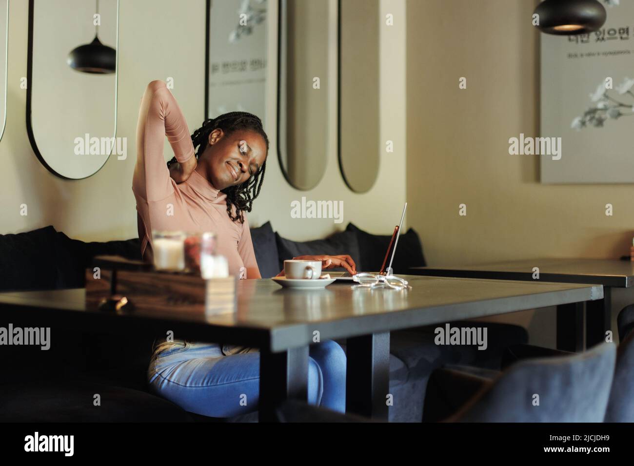 Femme d'affaires, anxieuse et fatiguée, mal de race mixte, tenir le cou, sentir la douleur, en utilisant l'ordinateur portable dans le café. Mauvaise posture, scoliose Banque D'Images