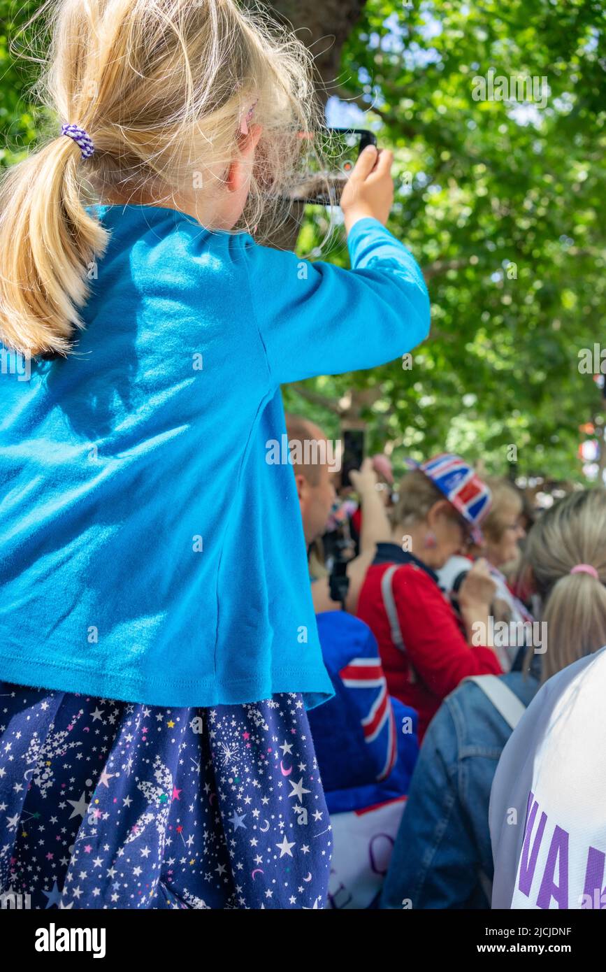 Jeune fille aux cheveux blonds assise sur ses épaules de pères filmant avec un iphone sur le Mall à Londres, Angleterre. Banque D'Images