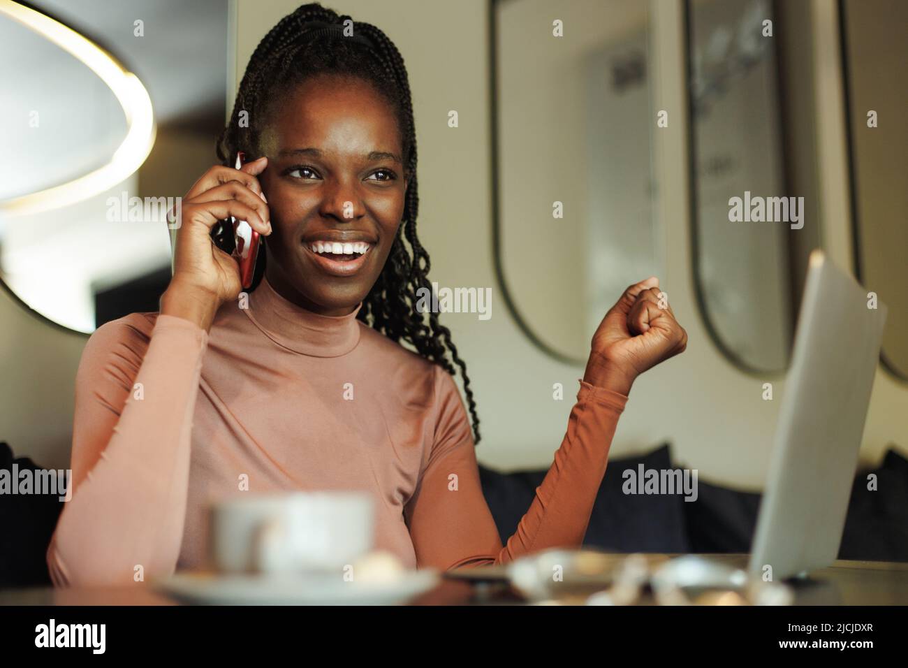 Riant, femme afro-américaine souriante et tortante, blogueur, buvez du café, parlez par téléphone avec vos collègues, travaillez en ligne au café Banque D'Images