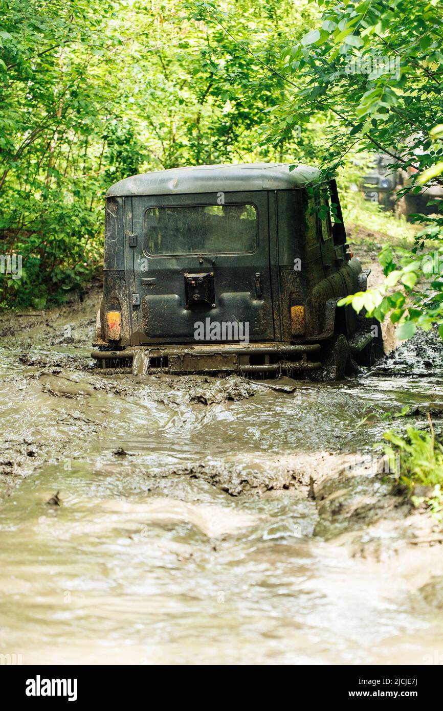 Vue arrière du véhicule utilitaire vert russe hors route UAZ Hunter s'est effondré, coincé sur une route sale dans la forêt parmi les arbres. Banque D'Images