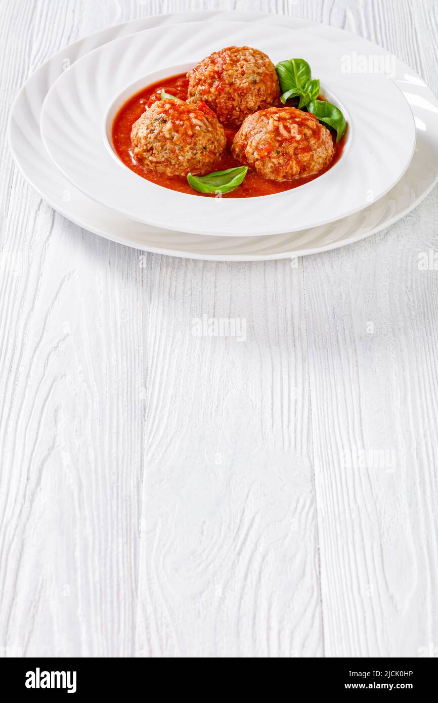 Boulettes de porc-épic italien, boulettes de viande de bœuf haché et de riz, sauce tomate, feuilles de basilic dans un bol blanc, sur une table en bois blanc, vue verticale de l'abov Banque D'Images