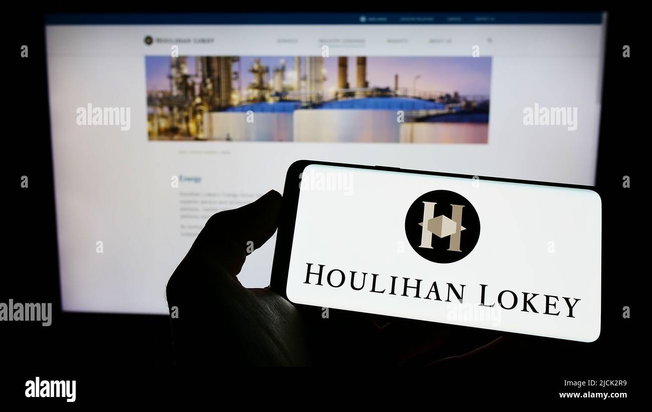Personne tenant un téléphone mobile avec le logo de la société d'investissement américaine Houlihan Lokey Inc. À l'écran en face de la page Web. Mise au point sur l'affichage du téléphone. Banque D'Images
