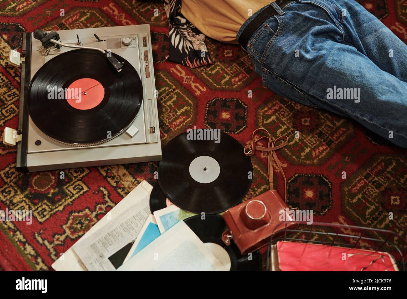 Une partie de jeune homme en jeans bleus se détendant sur le tapis rouge sur le sol et écoutant des disques vynil avec sa musique préférée Banque D'Images