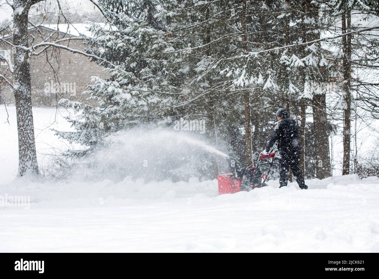 Homme utilisant une souffleuse à neige pour dégager l'allée lors d'une journée de neige. Banque D'Images