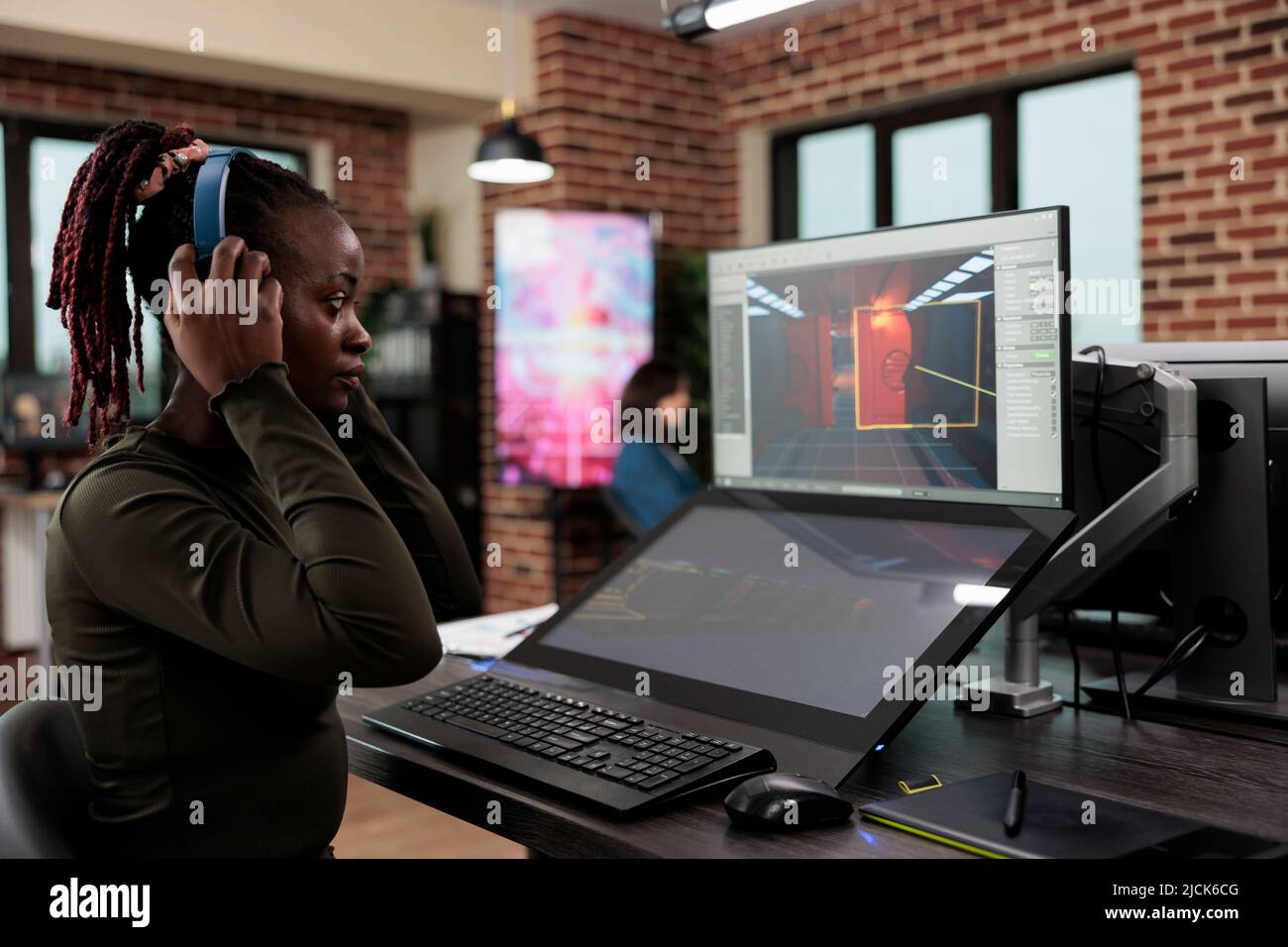 Artiste de jeu dans un espace de travail de bureau assis au bureau tout en travaillant sur l'interface de jeu. Niveau employé du département de conception portant des écouteurs sans fil lors de l'analyse de l'environnement numérique Banque D'Images
