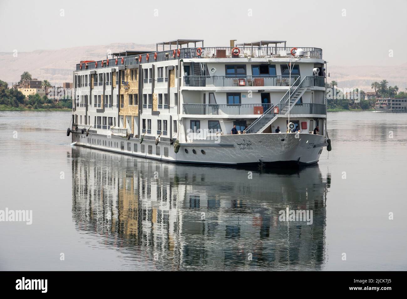 Bateau de croisière sur le Nil naviguant à un angle de 45% vers la caméra sur l'eau calme avec des réflexions dans la lumière du matin tôt Banque D'Images