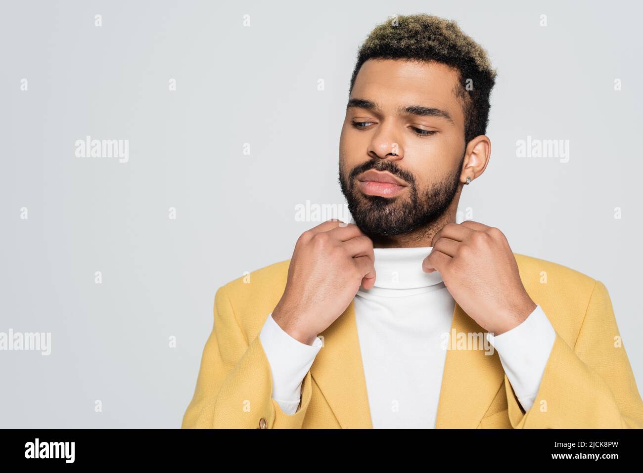 homme afro-américain barbu dans un blazer élégant qui ajuste le col de polo isolé sur le gris Banque D'Images