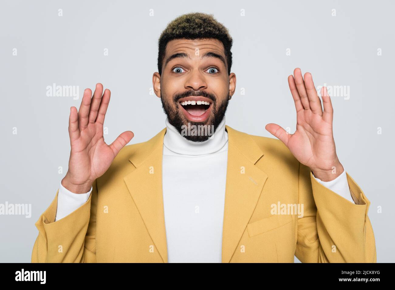 homme afro-américain excité dans un blazer jaune et col de polo isolé sur le gris Banque D'Images