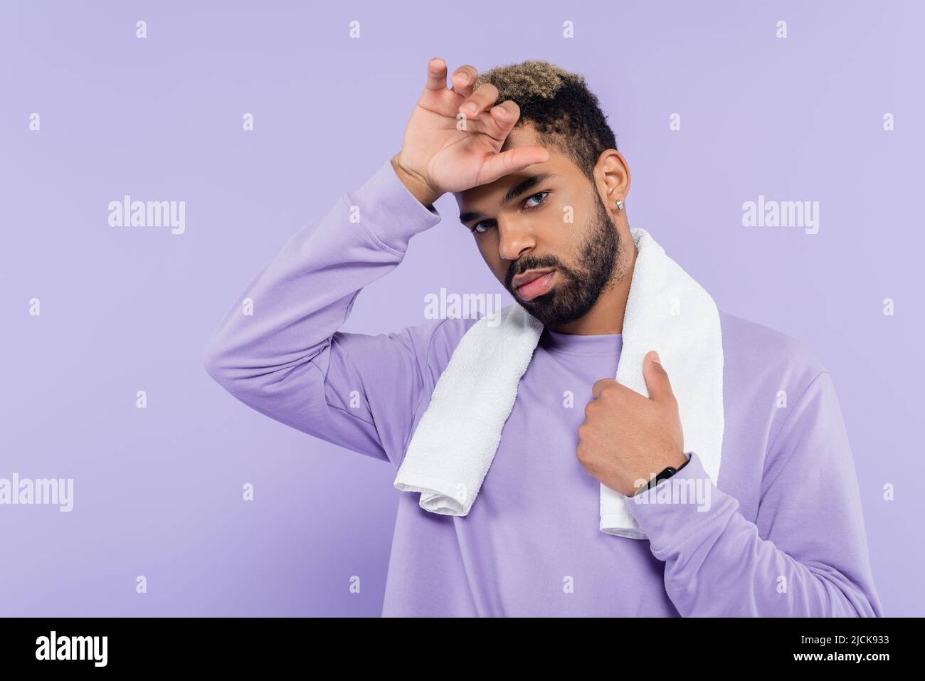 homme afro-américain fatigué en chandail tenant une serviette blanche et essuyant la sueur avec la main isolée sur le violet Banque D'Images