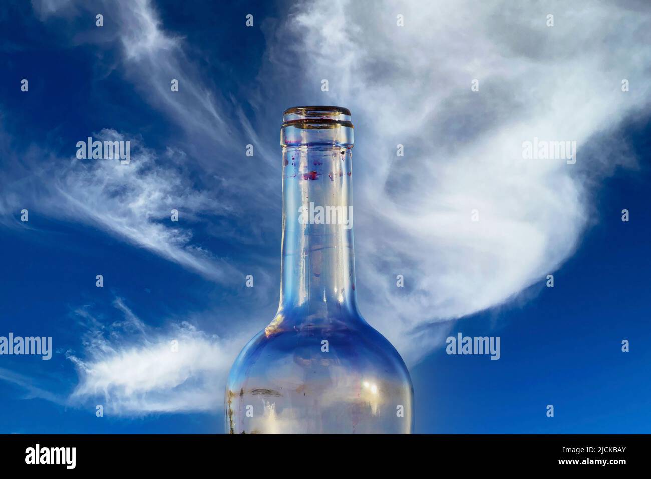 Gros plan d'une seule bouteille de verre d'alcool à vin rouge transparent isolée, ciel bleu clair et fond de nuage blanc moelleux Banque D'Images