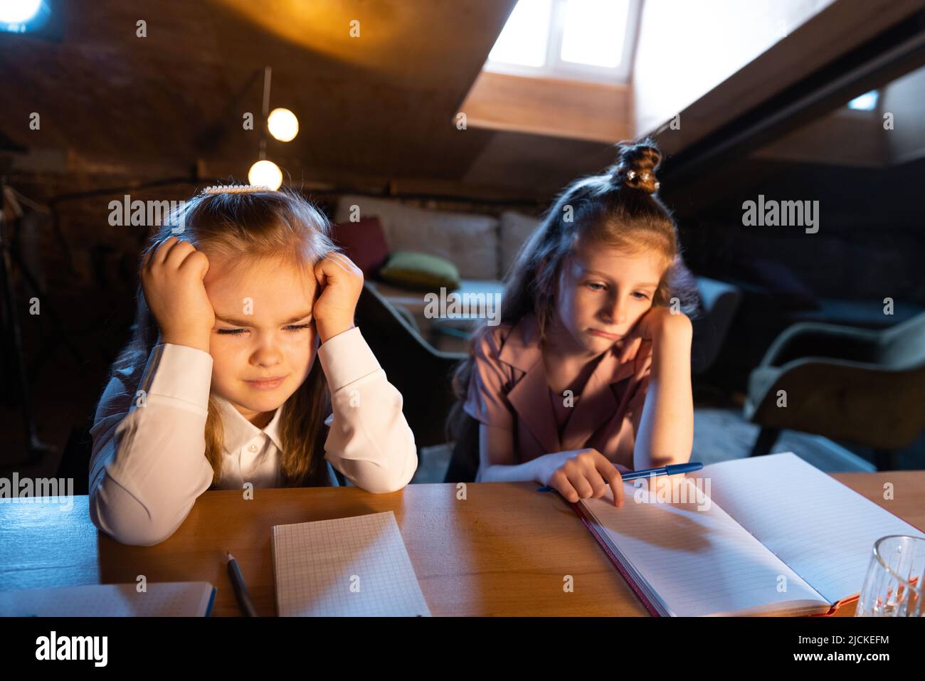 Portrait en direct des enfants mignons, des sœurs assis à la maison faisant leurs devoirs avec un ami le soir. Éducation en ligne, enfance, famille, apprentissage à distance Banque D'Images