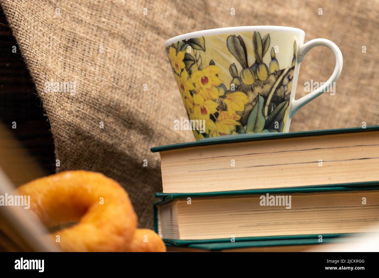Une tasse de thé fort sur une soucoupe, des beignets sur une assiette et une pile de livres sur la table. Banque D'Images