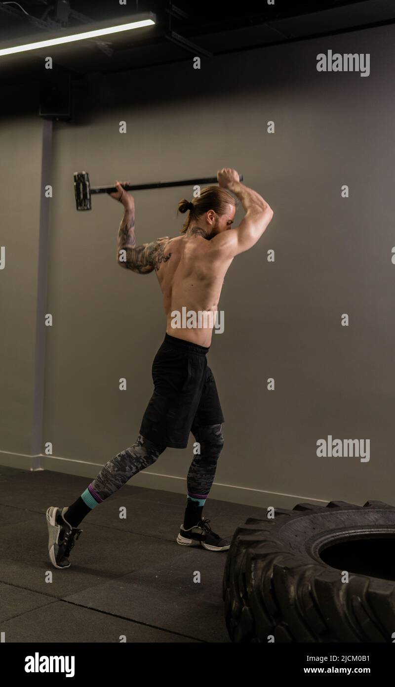 Pneu marteau musculaire crossfit roue traineau homme frapper sportif athlète, concept force lourde de forte de bodybuilder frapper, santé physique. Sombre Banque D'Images