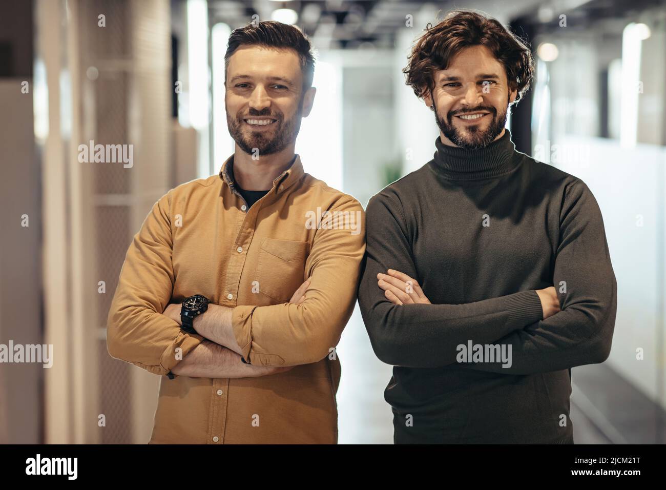 Portrait de deux entrepreneurs joyeux posant avec des bras croisés et souriant à la caméra dans le hall de l'entreprise. Concept de coworking Banque D'Images