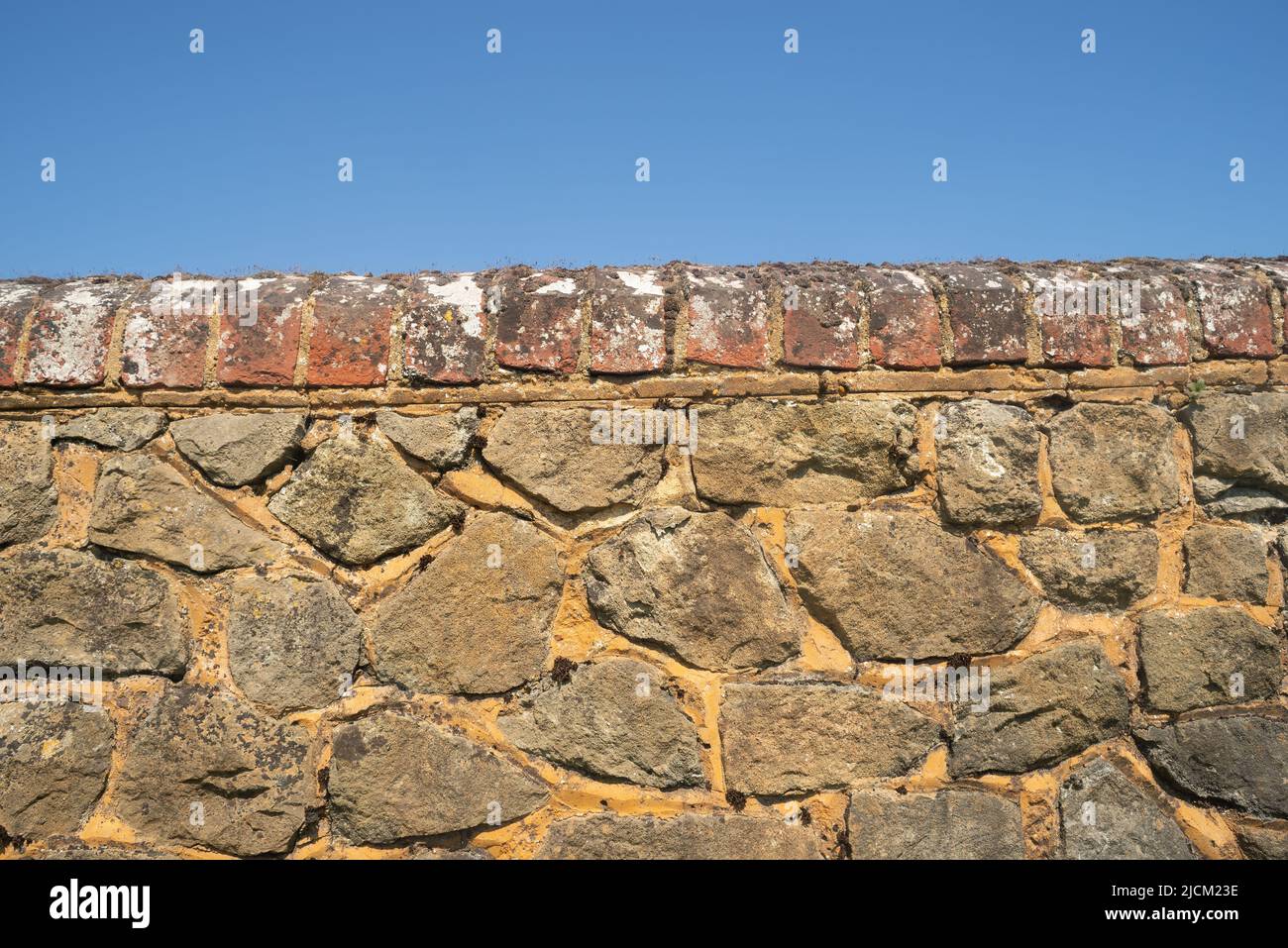 Kentish ragstone calcaire gris dur utilisé pour construire un mur frontière fort avec la brique rouge et le lichen sur le dessus contre un ciel bleu Banque D'Images