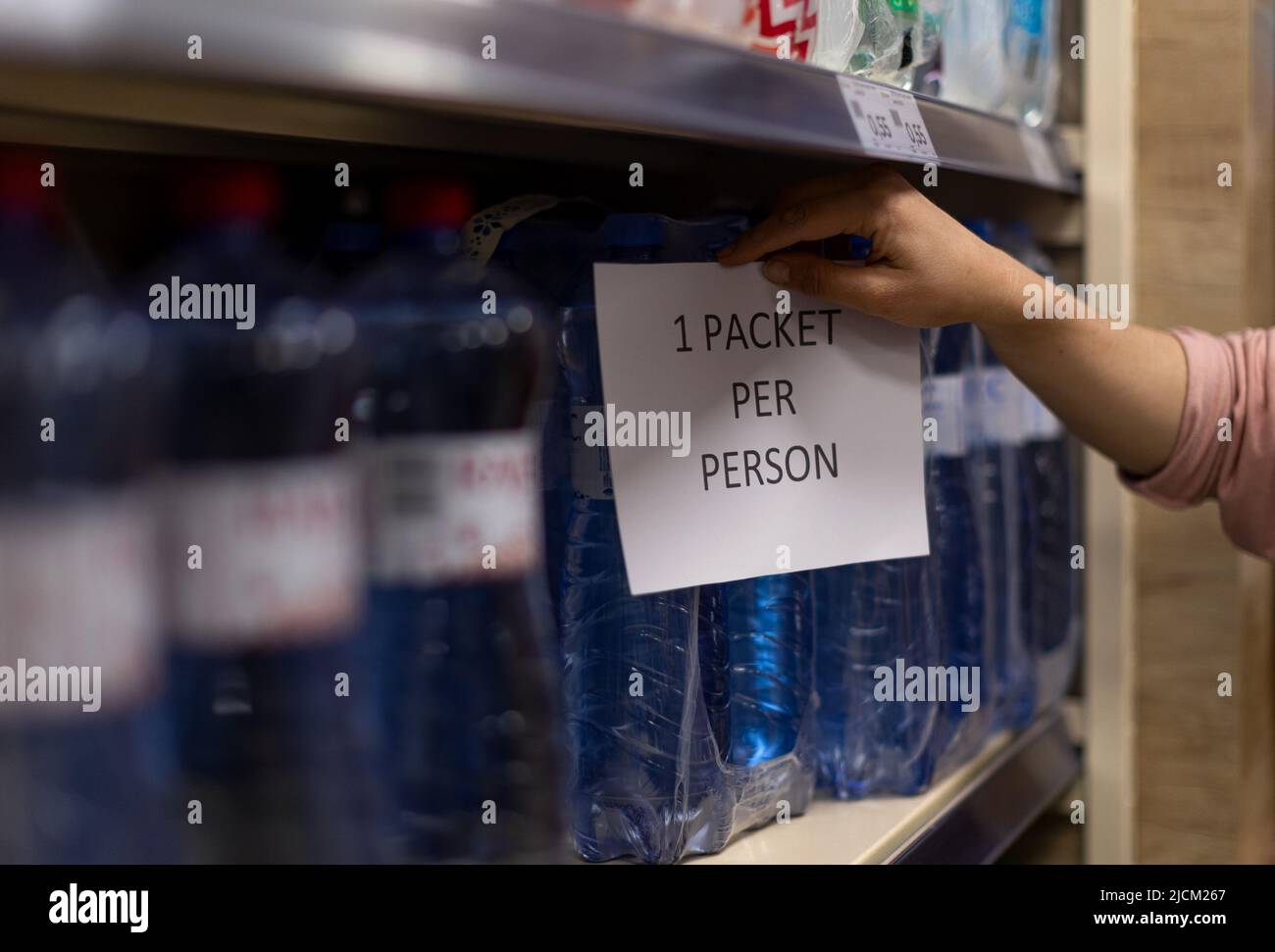 Femme prend l'eau minérale des étagères superaket, ventes limitées à un paquet par personne pendant la crise. Banque D'Images