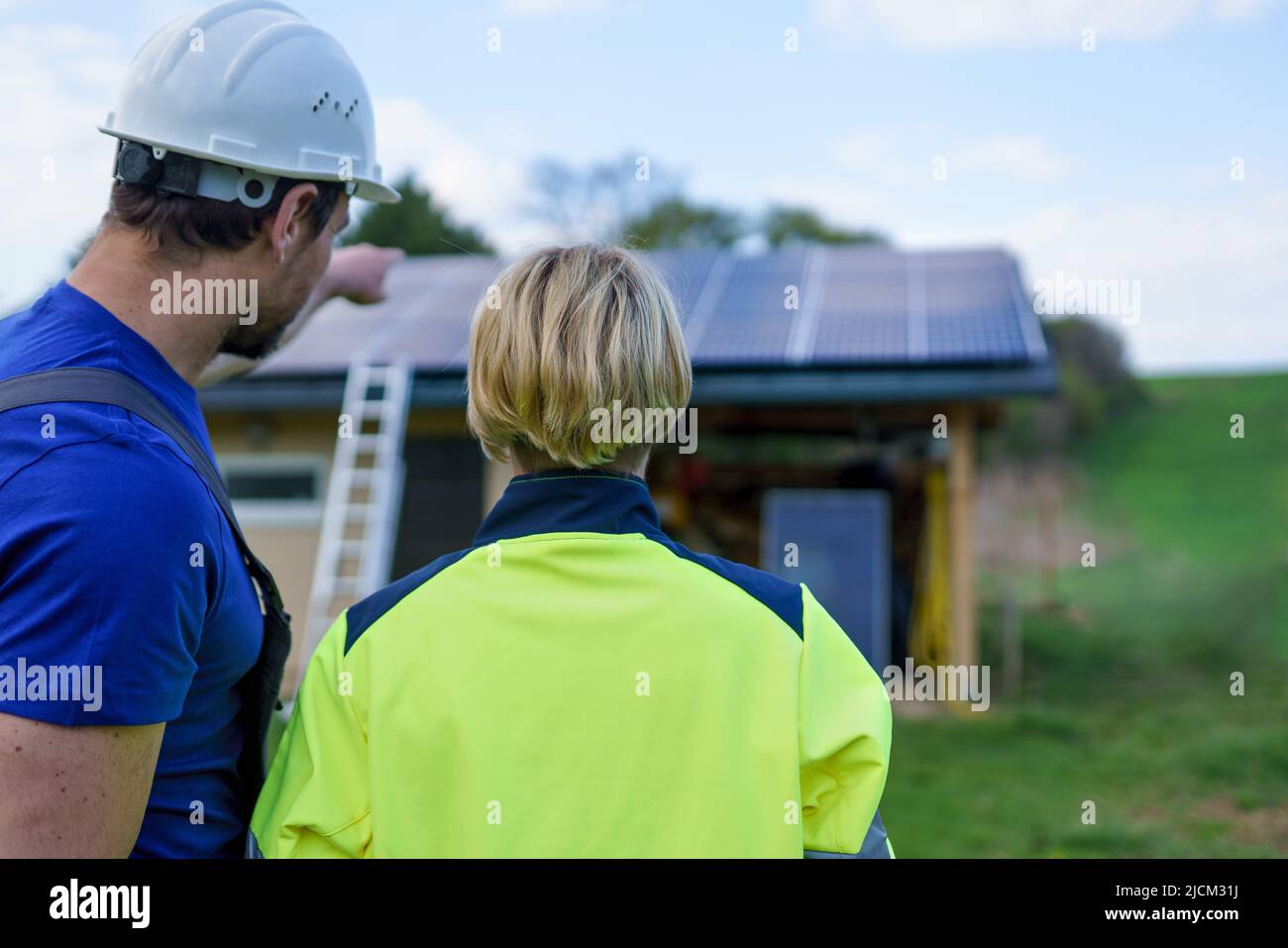 Homme et femme installateurs solaires ingénieurs avec la tablette tout en installant le système de panneau solaire sur la maison, vue arrière. Banque D'Images