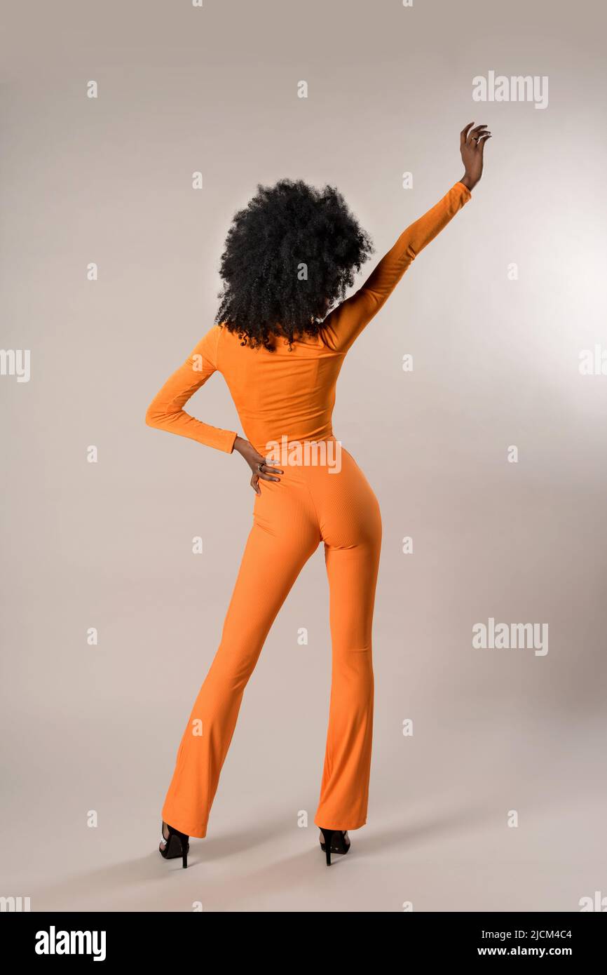 Vue arrière du corps entier d'une femme afro-américaine mince anonyme en costume serré debout sur fond blanc avec bras relevé en studio Banque D'Images