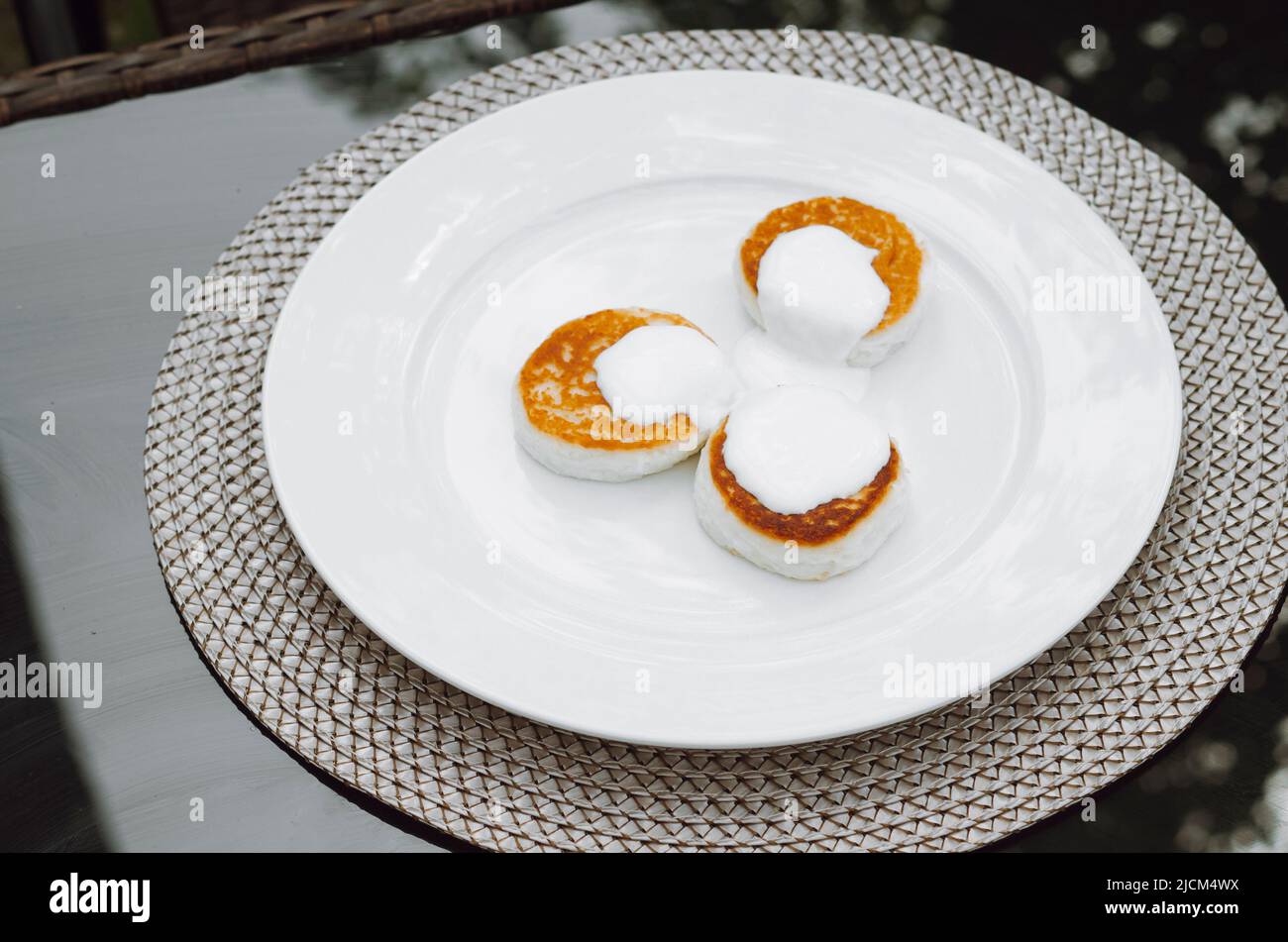 Beignets de fromage cottage Syrniki servi avec de la crème sure sur une assiette blanche. Dessert caillé pour le petit déjeuner. Banque D'Images