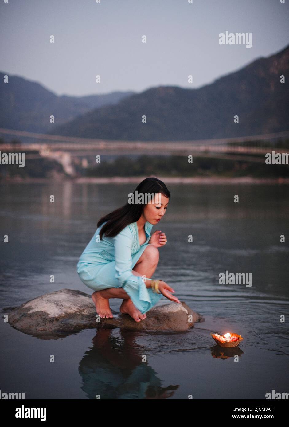 Une femme fait une offrande florale à la rivière Ganges au crépuscule à Rishikesh, Uttarakhand, Inde. Banque D'Images