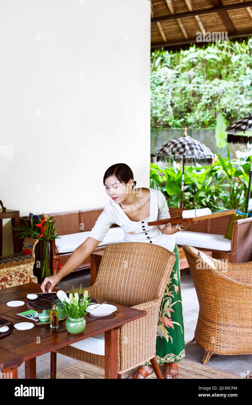 Une serveuse balinaise qui place la table pour le déjeuner au Diatas Pohon café, Ubud Hanging Gardens, Bali, Indonésie. Banque D'Images
