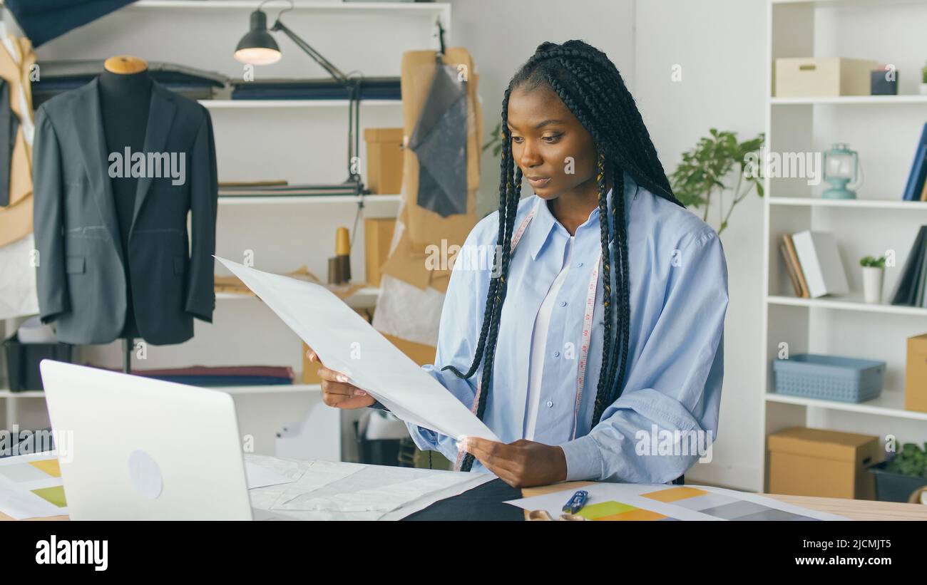 Un talentueux designer de mode afro-américain crée une nouvelle collection de mode tout en travaillant sur un ordinateur portable dans un studio Fashion Business Startup. Concept Banque D'Images