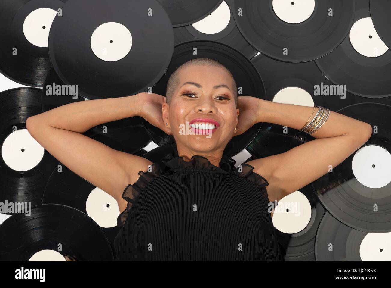 Concept de loisirs et de musique. Portrait de la belle femme thaïlandaise couché sur fond de vinyle noir avec le sourire. Modèle avec tête rasée, port de blou noir Banque D'Images