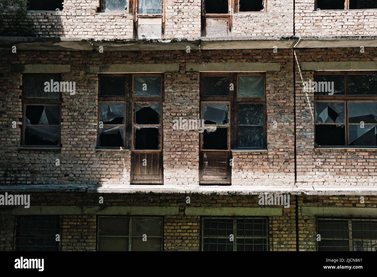 Le mur d'un vieux bâtiment abandonné en briques avec des fenêtres cassées. Banque D'Images