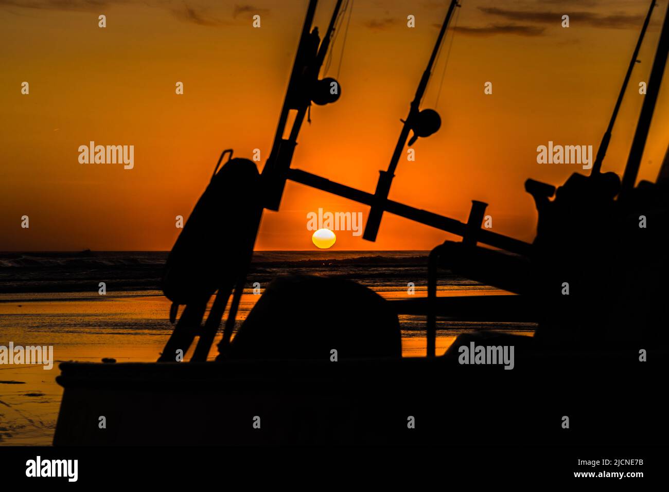Silhouette d'un bateau de pêche avec cannes à pêche et moulinets avec un coucher de soleil doré. Banque D'Images