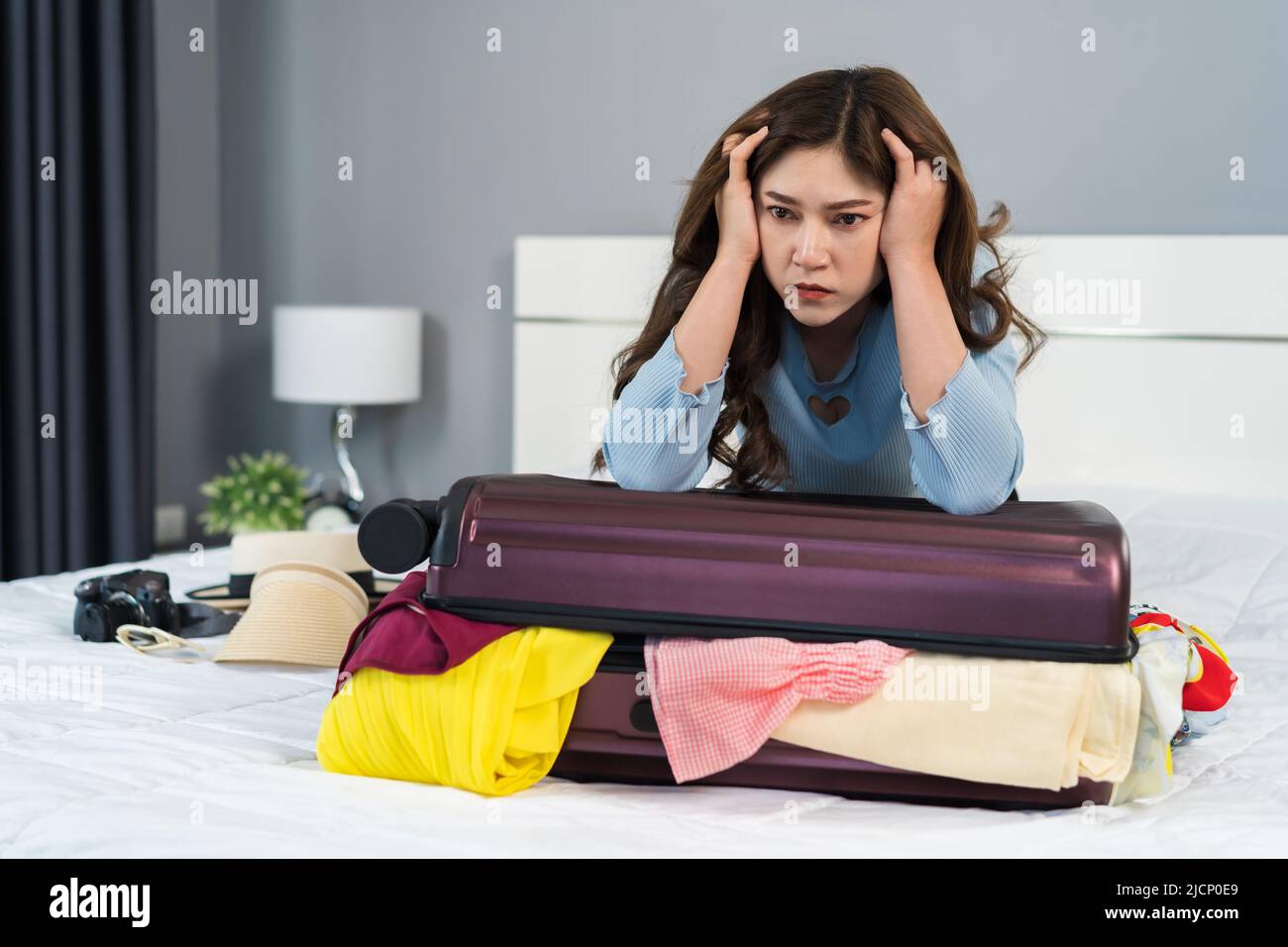 jeune femme essayant de fermer une valise surremplie sur son lit Banque D'Images