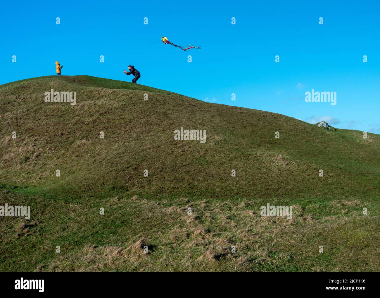 Wiltshire,Angleterre,UK-18 février 2021: Un petit garçon regarde son père courir le long du haut de la longue barrow néolithique balayée par le vent, traînant un cerf-volant Banque D'Images